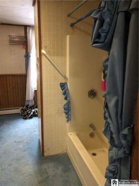 bathroom featuring wood walls, shower / bathtub combination with curtain, and a baseboard heating unit