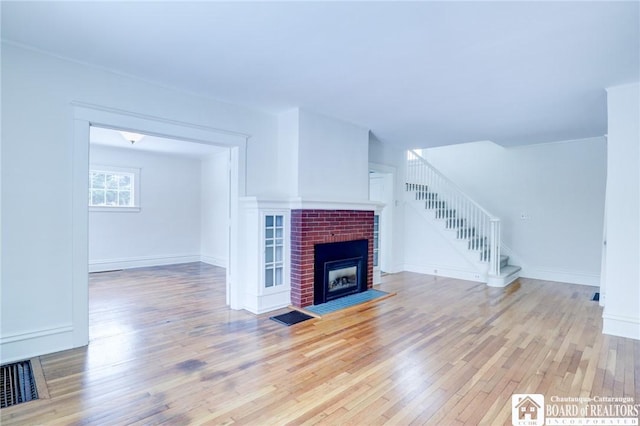 unfurnished living room with light wood-type flooring and a brick fireplace