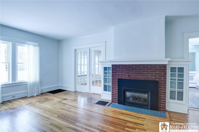 unfurnished living room with french doors, hardwood / wood-style floors, and a brick fireplace