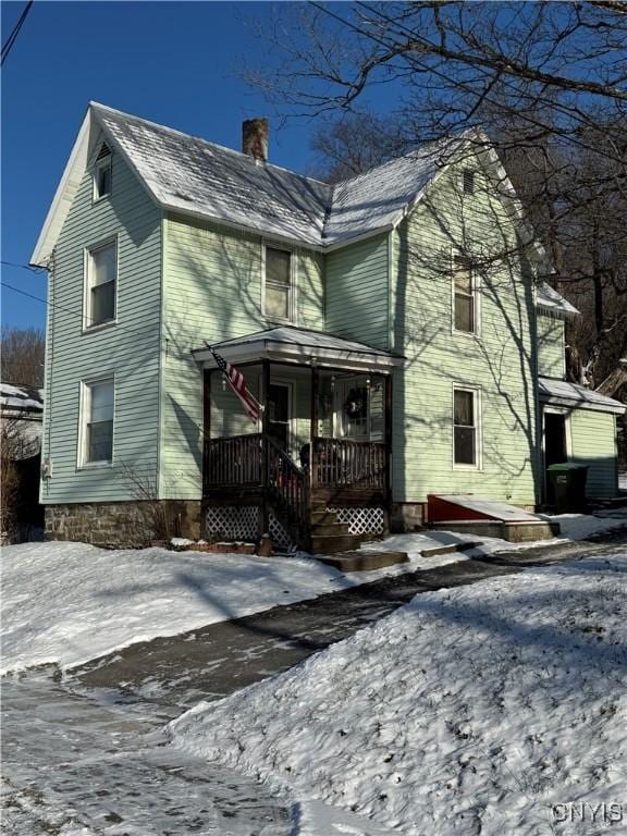 snow covered rear of property featuring a porch