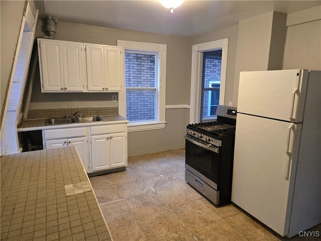 kitchen featuring white cabinetry, stainless steel range with gas stovetop, sink, and white refrigerator