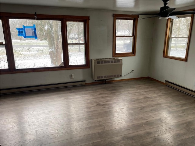 unfurnished room with ceiling fan, wood-type flooring, an AC wall unit, and a baseboard heating unit