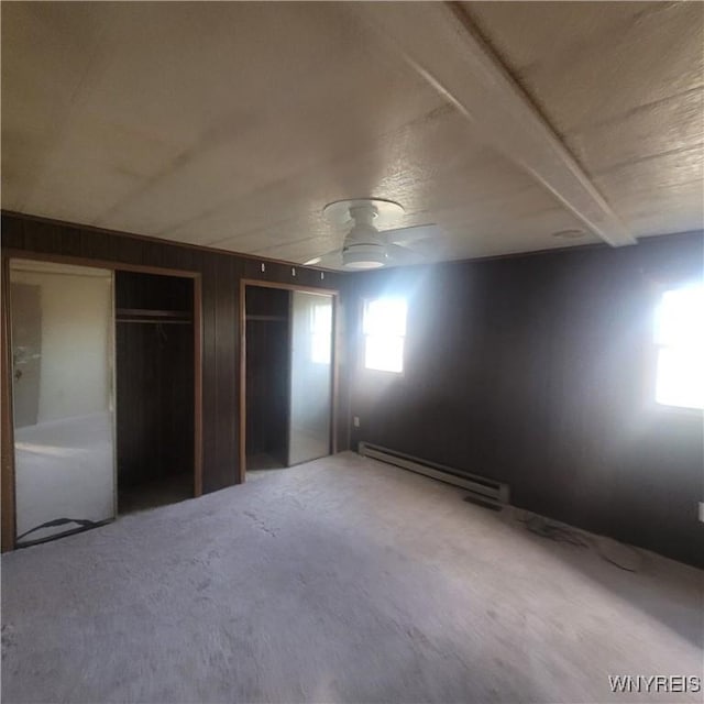 unfurnished bedroom featuring baseboard heating, multiple closets, ceiling fan, and wood walls