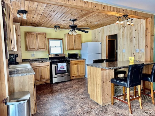 kitchen with sink, stainless steel range oven, a kitchen bar, wooden walls, and ceiling fan with notable chandelier