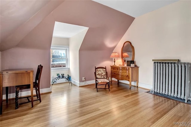 living area featuring radiator heating unit, light hardwood / wood-style floors, and vaulted ceiling