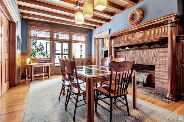 dining room featuring beam ceiling, wood walls, and light hardwood / wood-style flooring