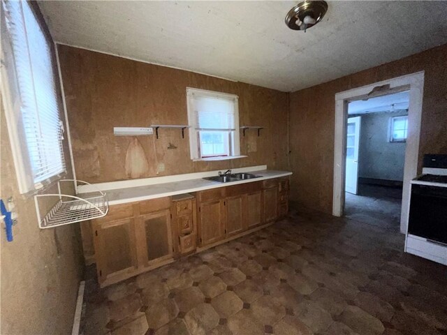 kitchen featuring white range with electric stovetop, wood walls, sink, and a healthy amount of sunlight