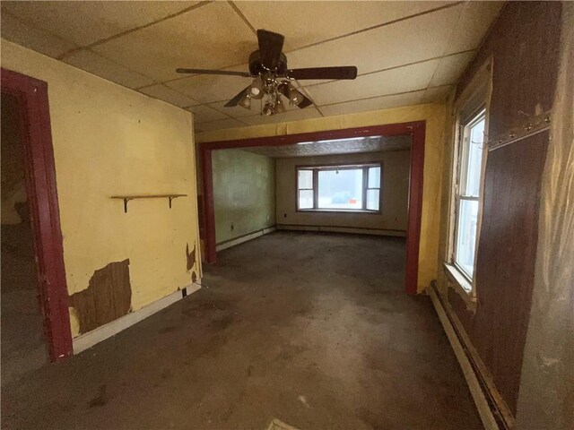 unfurnished room featuring a drop ceiling, ceiling fan, and a baseboard radiator