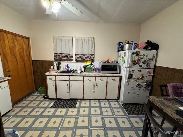 kitchen with ceiling fan, sink, white cabinets, white fridge, and wood walls