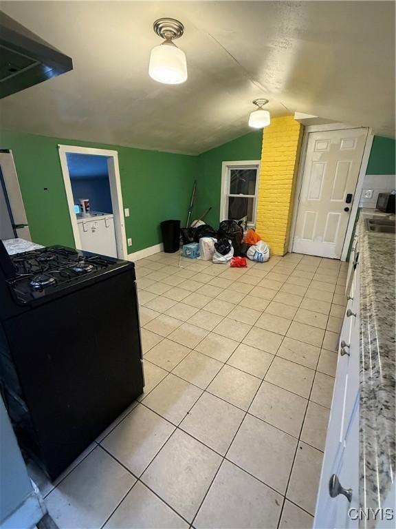 kitchen with light tile patterned floors, lofted ceiling, white cabinetry, and black range oven