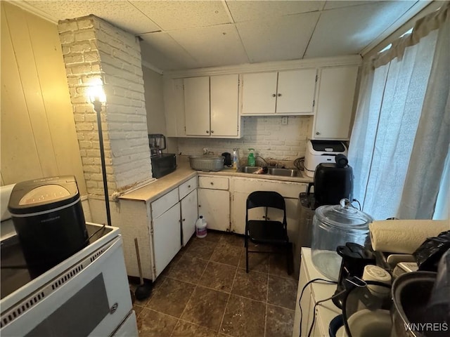 kitchen with white cabinetry, sink, a drop ceiling, and range