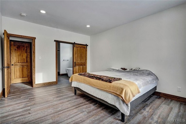 bedroom with connected bathroom, a barn door, and hardwood / wood-style floors