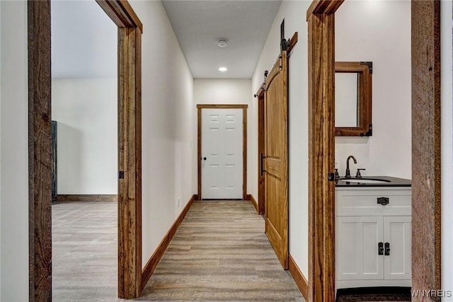 hall with light wood-type flooring, a barn door, and sink