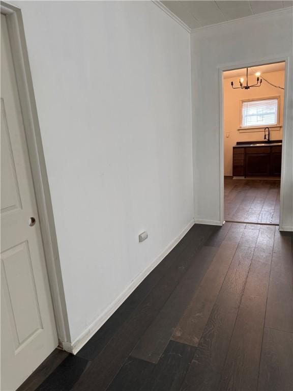 empty room with a notable chandelier, ornamental molding, a sink, dark wood-style floors, and baseboards