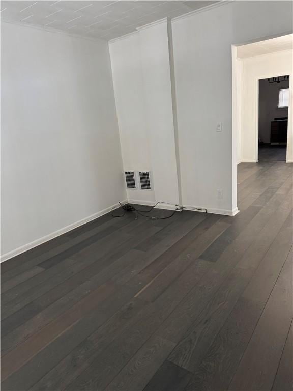 empty room featuring dark wood-style floors, visible vents, and baseboards