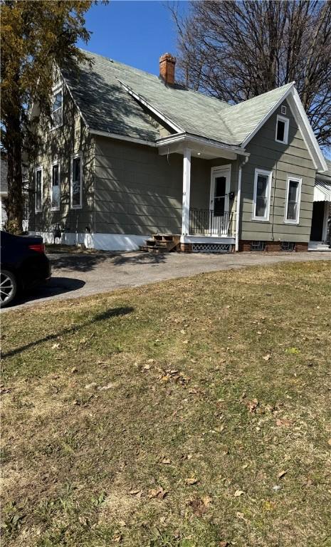 back of house with a porch, a yard, an attached garage, and a chimney