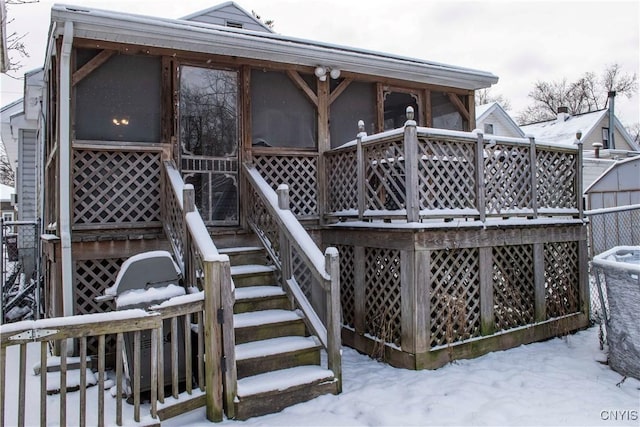 snow covered back of property with a sunroom