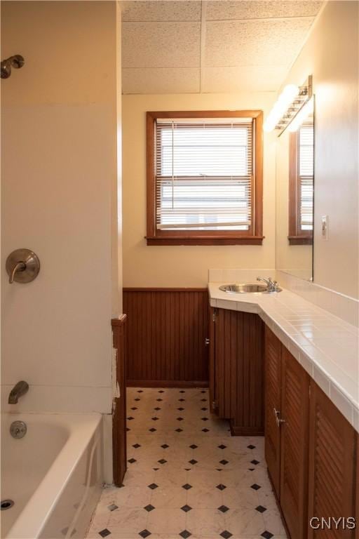 bathroom with a paneled ceiling, vanity, wooden walls, and bathtub / shower combination