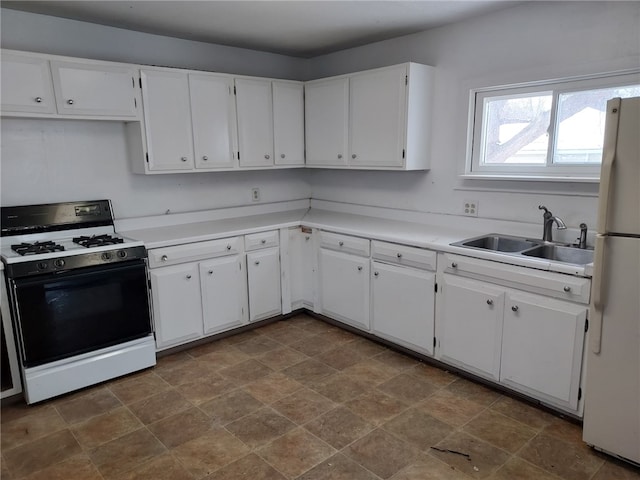 kitchen with gas range, white refrigerator, sink, and white cabinets