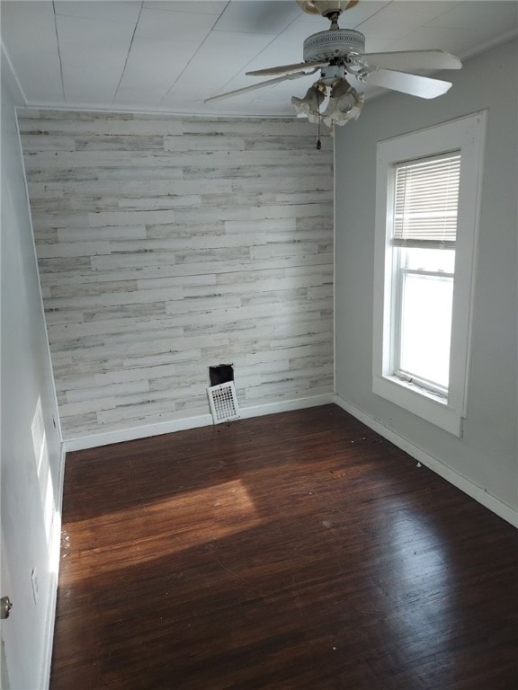 unfurnished room with dark wood-type flooring, ceiling fan, and wood walls