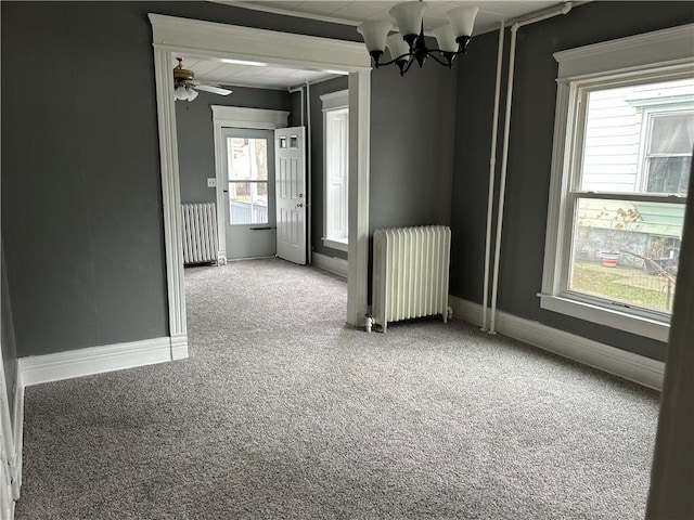 carpeted spare room featuring ceiling fan with notable chandelier and radiator heating unit