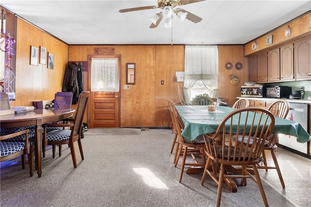 dining space with ceiling fan, light carpet, and wooden walls