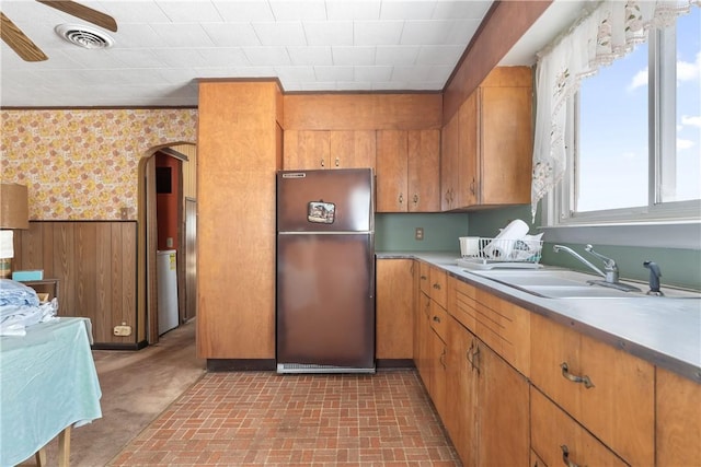 kitchen featuring stainless steel fridge, sink, crown molding, and wood walls