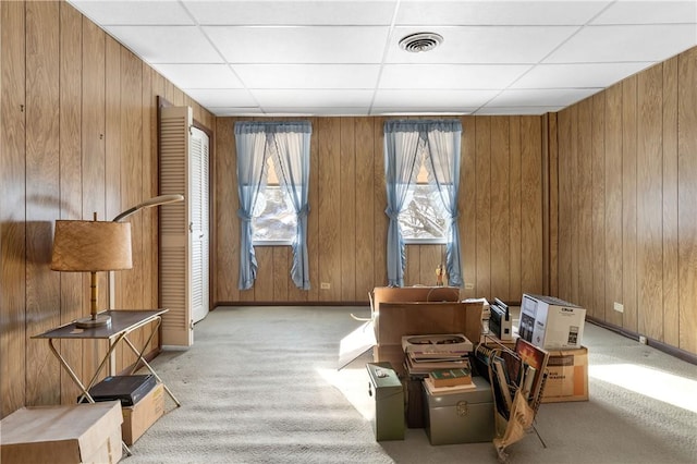 miscellaneous room with a drop ceiling, wood walls, and light colored carpet