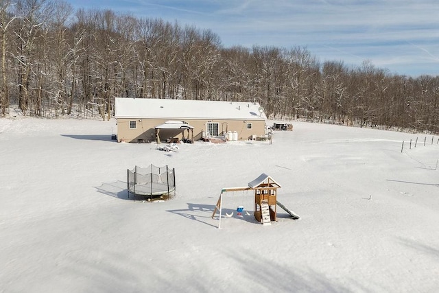 snow covered rear of property with a playground and a trampoline