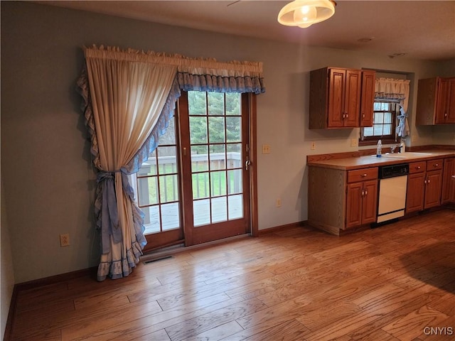 kitchen with a wealth of natural light, sink, white dishwasher, and light wood-type flooring