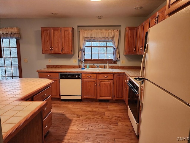 kitchen with white appliances, tile countertops, light hardwood / wood-style floors, and sink