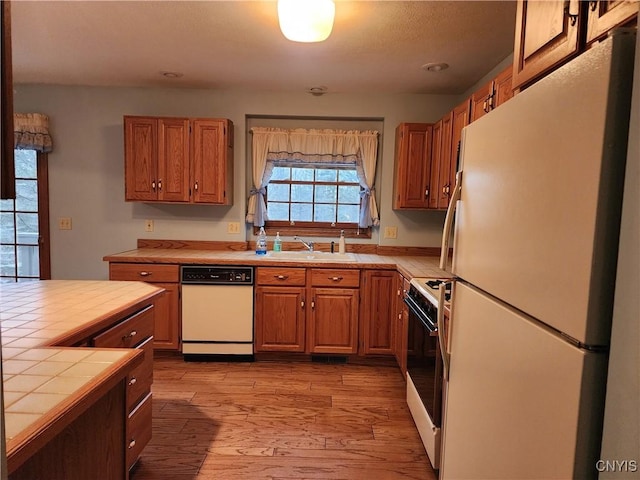 kitchen with white appliances, brown cabinetry, tile countertops, wood finished floors, and a sink