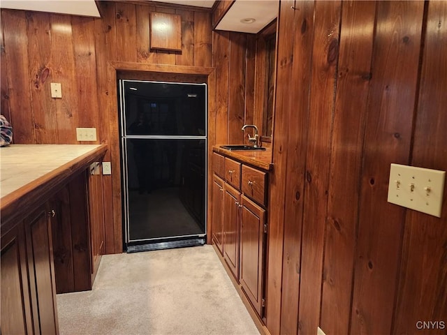 kitchen featuring tile countertops, light colored carpet, freestanding refrigerator, a sink, and wooden walls