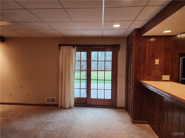 doorway with a paneled ceiling, carpet floors, and wooden walls