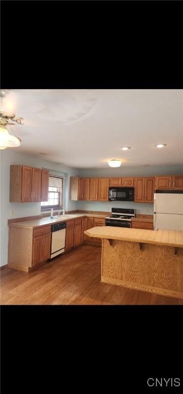 kitchen with white appliances, light wood-style flooring, brown cabinets, light countertops, and recessed lighting