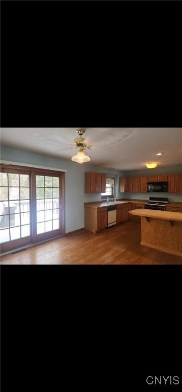 kitchen featuring brown cabinetry, dishwasher, light wood-style flooring, light countertops, and black microwave