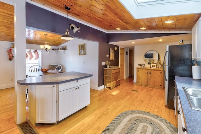 kitchen with light wood-style flooring, white cabinetry, lofted ceiling with skylight, dark countertops, and decorative light fixtures