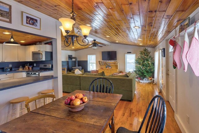 dining space with wood ceiling, light wood-style flooring, vaulted ceiling, and a wood stove