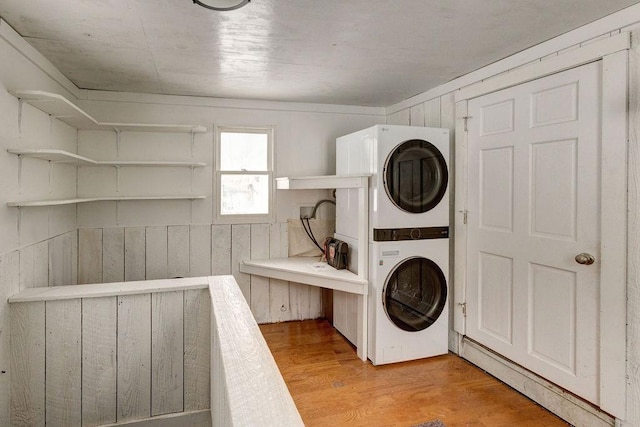 clothes washing area featuring laundry area, wood walls, stacked washer and clothes dryer, and light wood-style floors