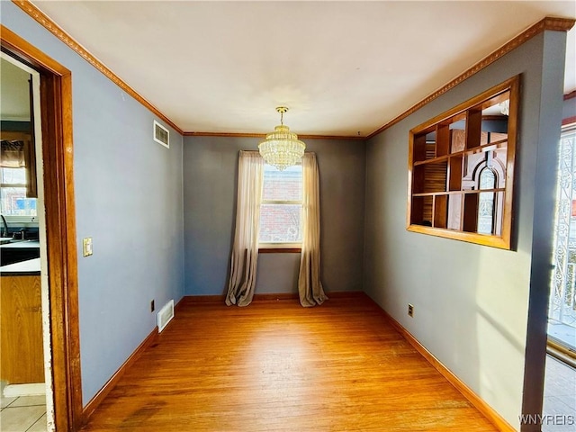 unfurnished dining area featuring crown molding, a chandelier, and light hardwood / wood-style floors