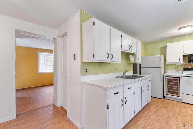 kitchen with stove, white refrigerator, sink, light wood-type flooring, and white cabinetry