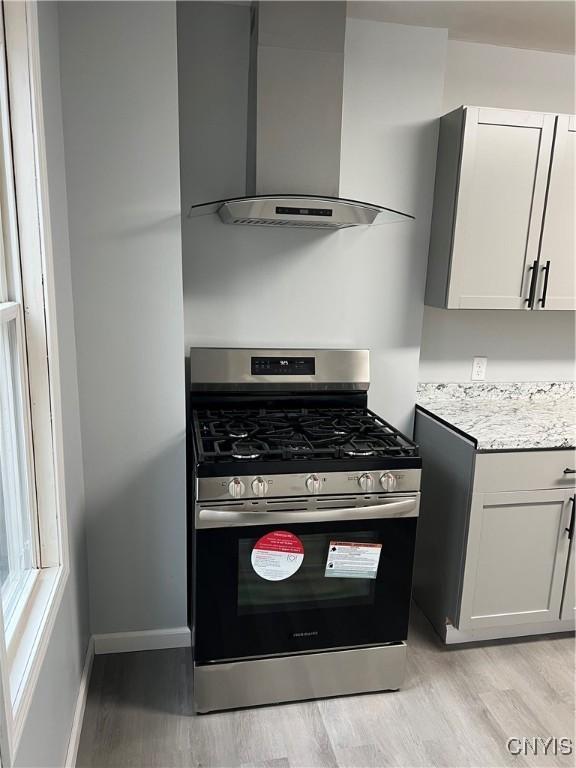 kitchen featuring wall chimney range hood, light stone counters, stainless steel range with gas cooktop, light hardwood / wood-style floors, and white cabinets