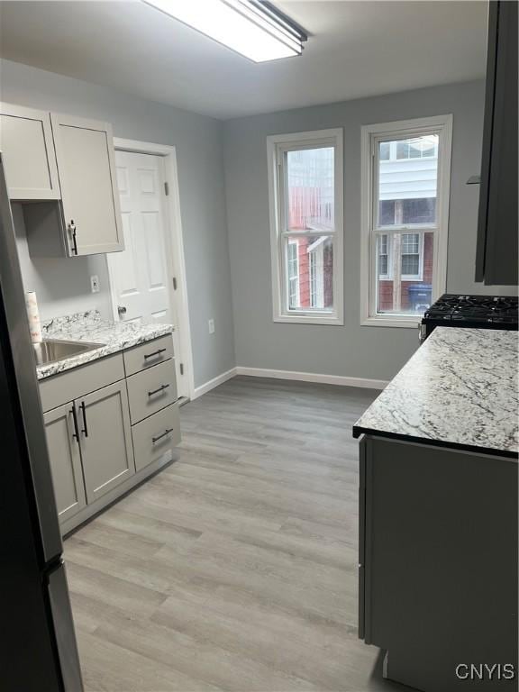 kitchen with stainless steel refrigerator, white cabinetry, sink, light stone counters, and light hardwood / wood-style flooring