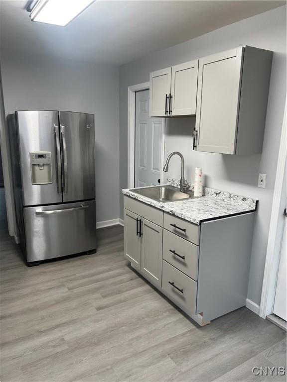 kitchen with light hardwood / wood-style floors, light stone counters, stainless steel fridge with ice dispenser, and sink