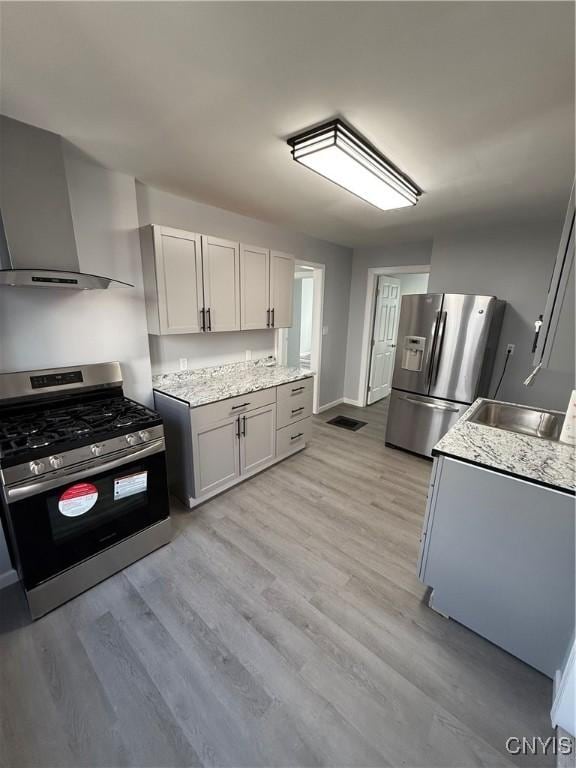 kitchen with light hardwood / wood-style flooring, wall chimney exhaust hood, gray cabinets, light stone countertops, and appliances with stainless steel finishes