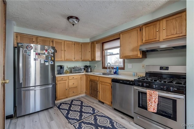 kitchen with a textured ceiling, stainless steel appliances, light hardwood / wood-style flooring, and sink