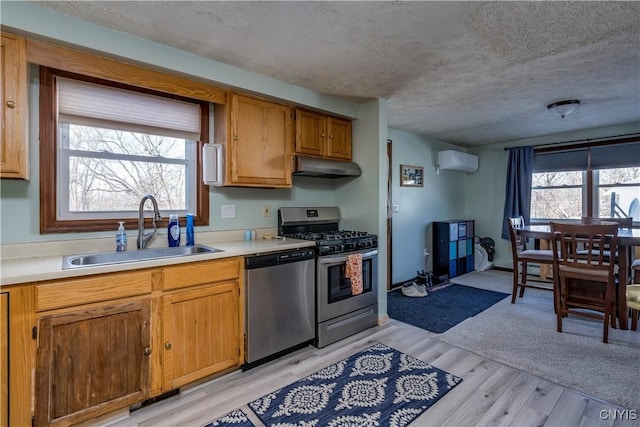 kitchen with a textured ceiling, stainless steel appliances, sink, an AC wall unit, and light hardwood / wood-style floors