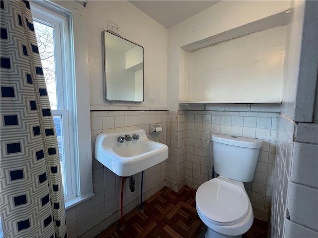 bathroom with sink, toilet, parquet floors, and tile walls