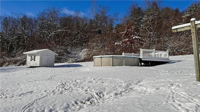 yard layered in snow featuring a shed, a deck, an outdoor pool, and an outbuilding