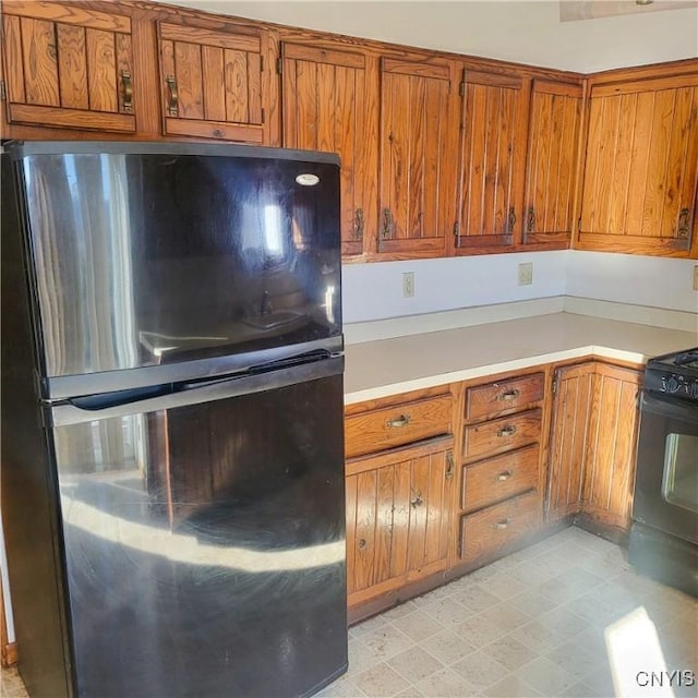 kitchen with brown cabinets, light floors, light countertops, stove, and freestanding refrigerator